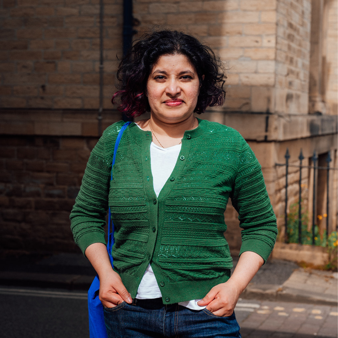Woman in green cardigan standing on a street.